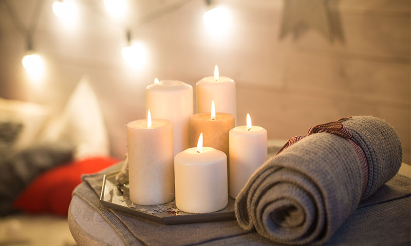 Various candles resting on a side table with a rolled up blanket - perfect decor to make a home feel warm. | SHW Blog