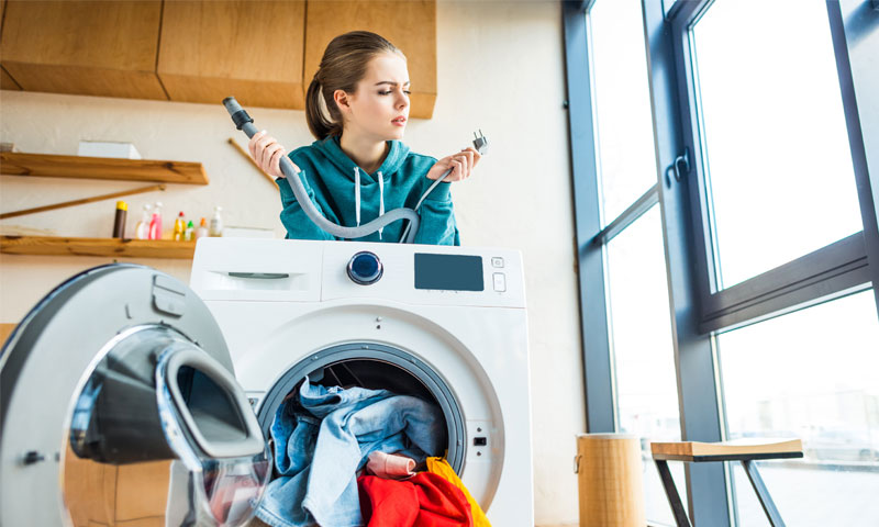 Young woman having trouble fixing her broken washing machine