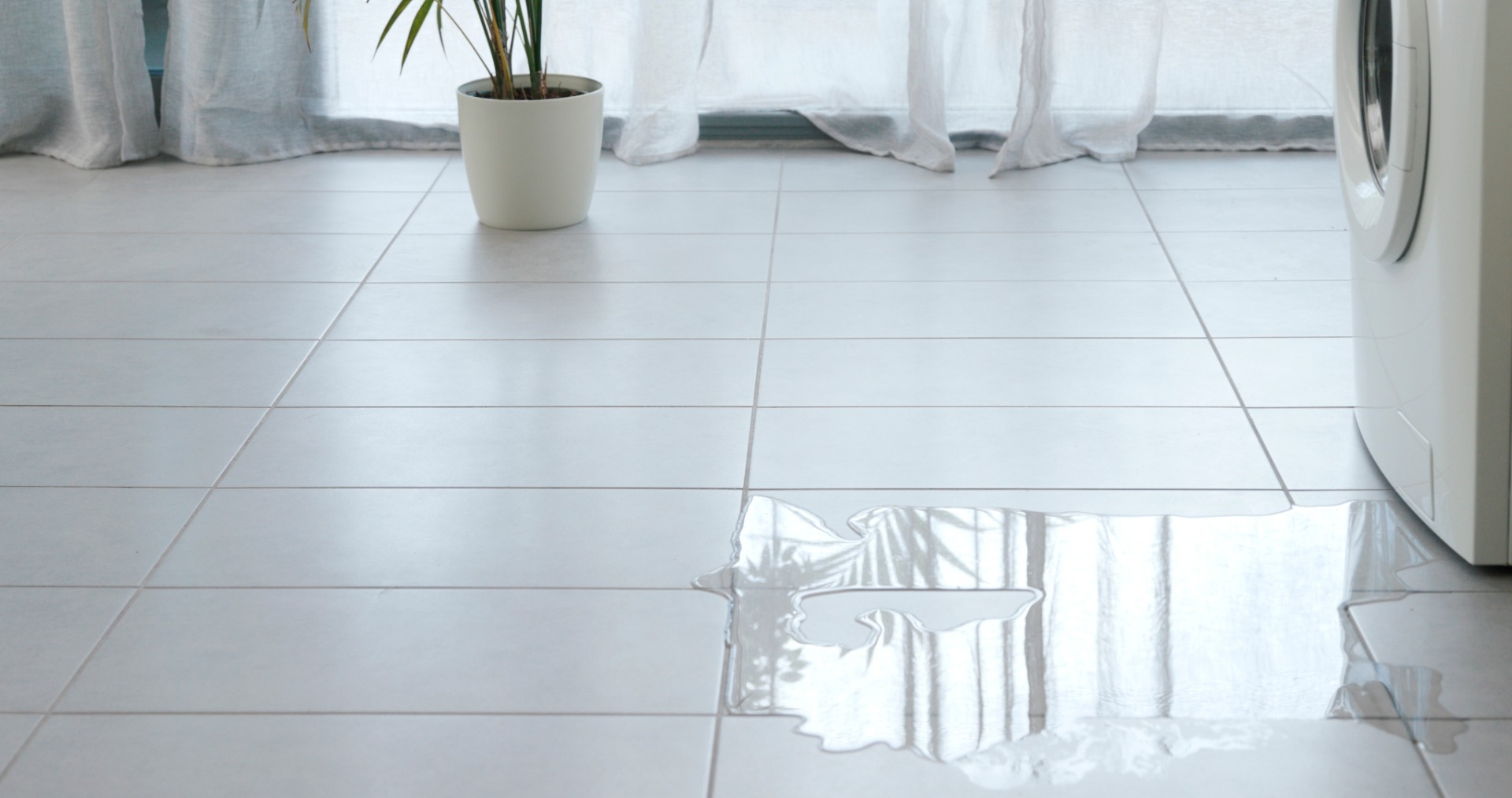 Clothes washing machine leaking onto a white tile floor.