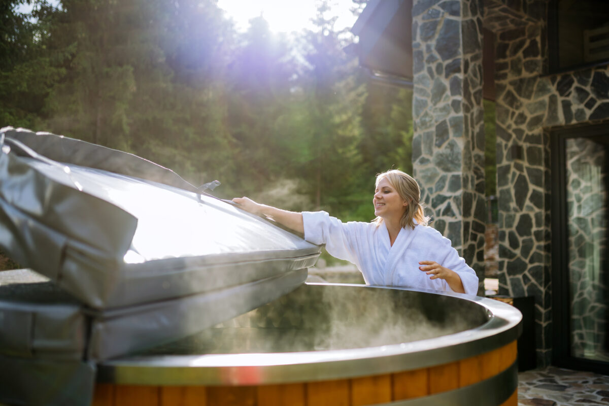 Woman in white bathrobe lifting the cover to a hot tub. | SHW Blog