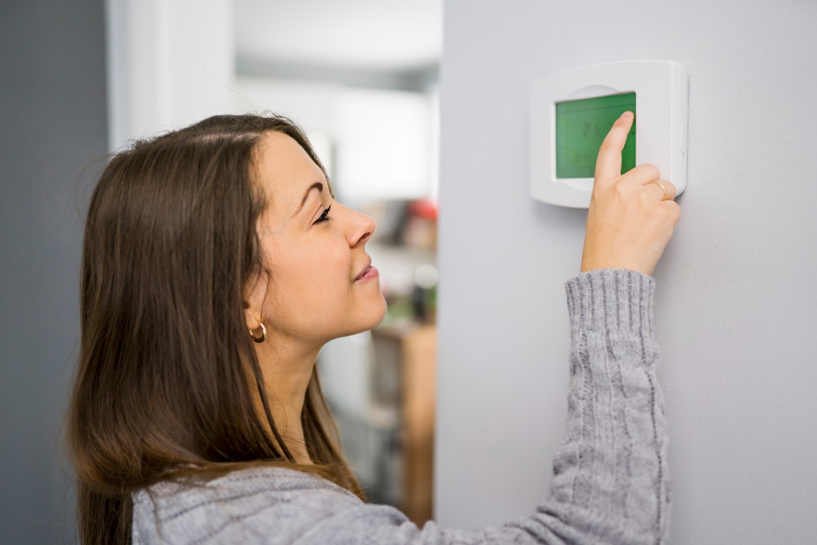 Smiling woman adjusting the settings on her digital thermostat to save money.