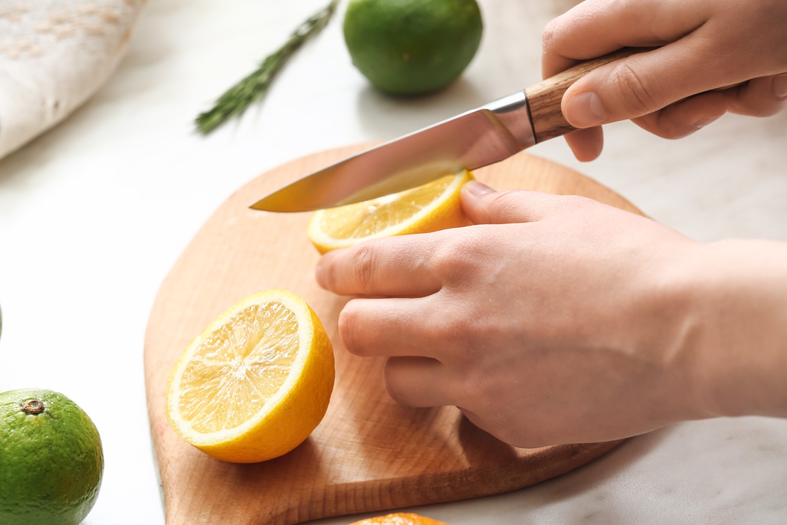 Hnads cutting lemons with a knife on a cutting board. Limes are off to the side.