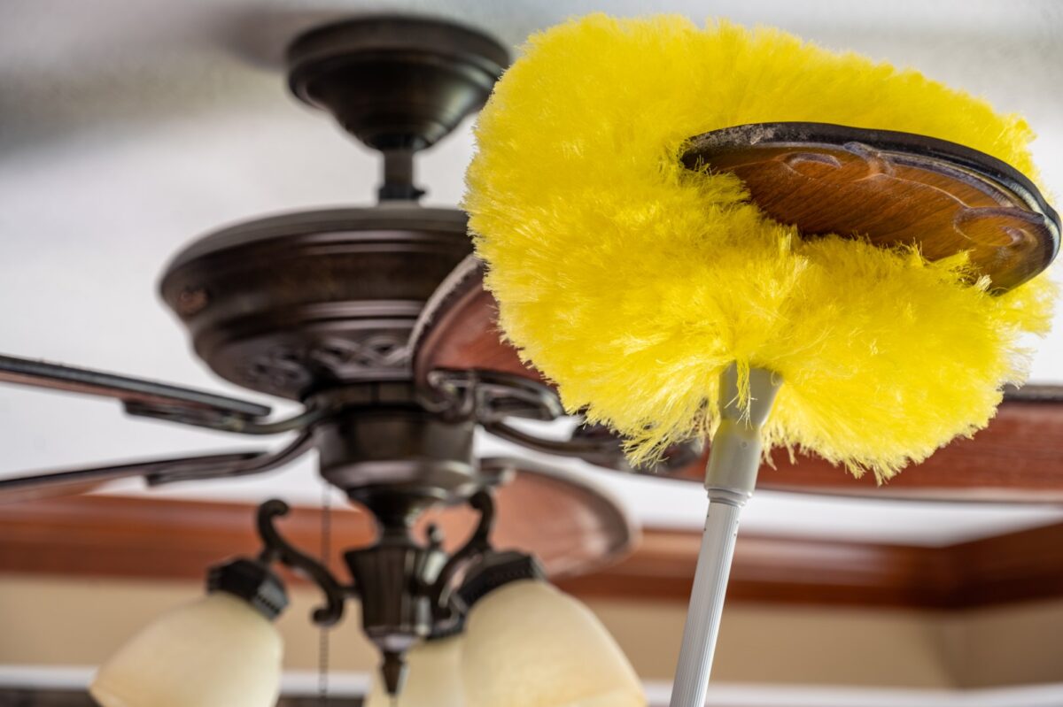 Using a wand feather duster to remove and clean dust from a ceiling fan.