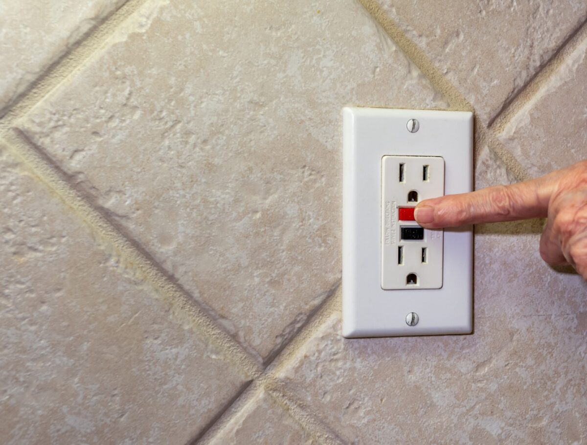 Closeup of hand resetting tripped GFCI outlet.