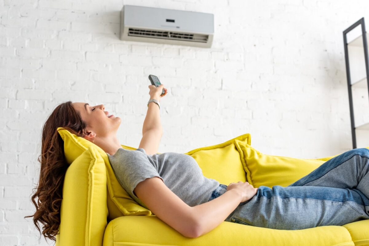 Woman relaxing under air conditioner and holding remote control.