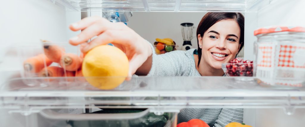 Smiling woman taking a fresh lemon out of the fridge thanks to her home warranty. | SHW Blog